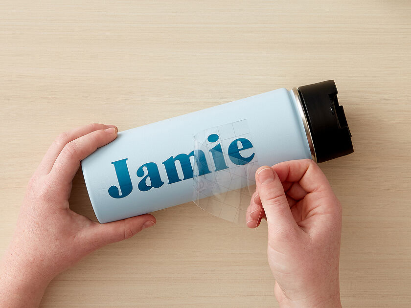 Woman's hands using transfer tape to adhere the blue vinyl onto a small drinking glass